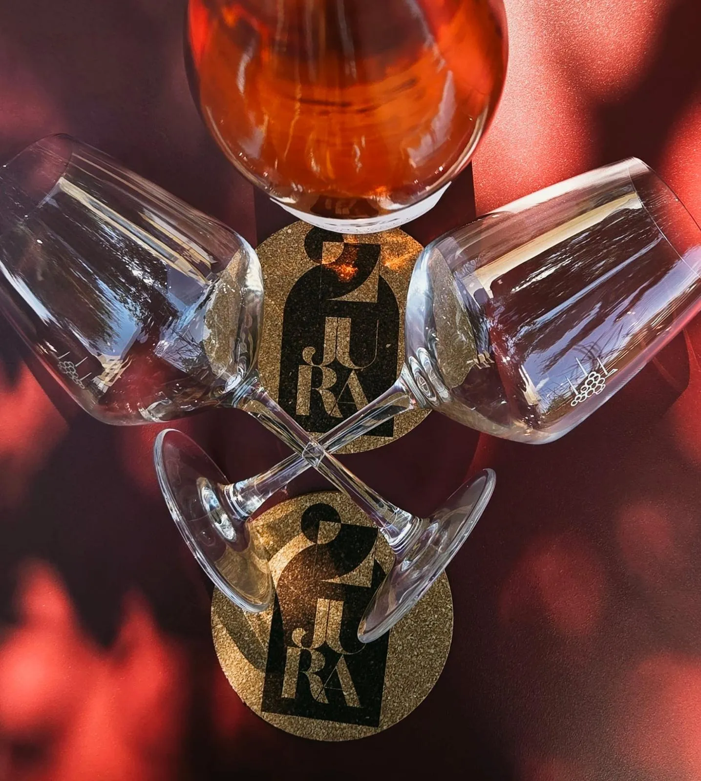 Deux verres et une bouteille disposés sur une table rouge avec les dessous de verre JuRa